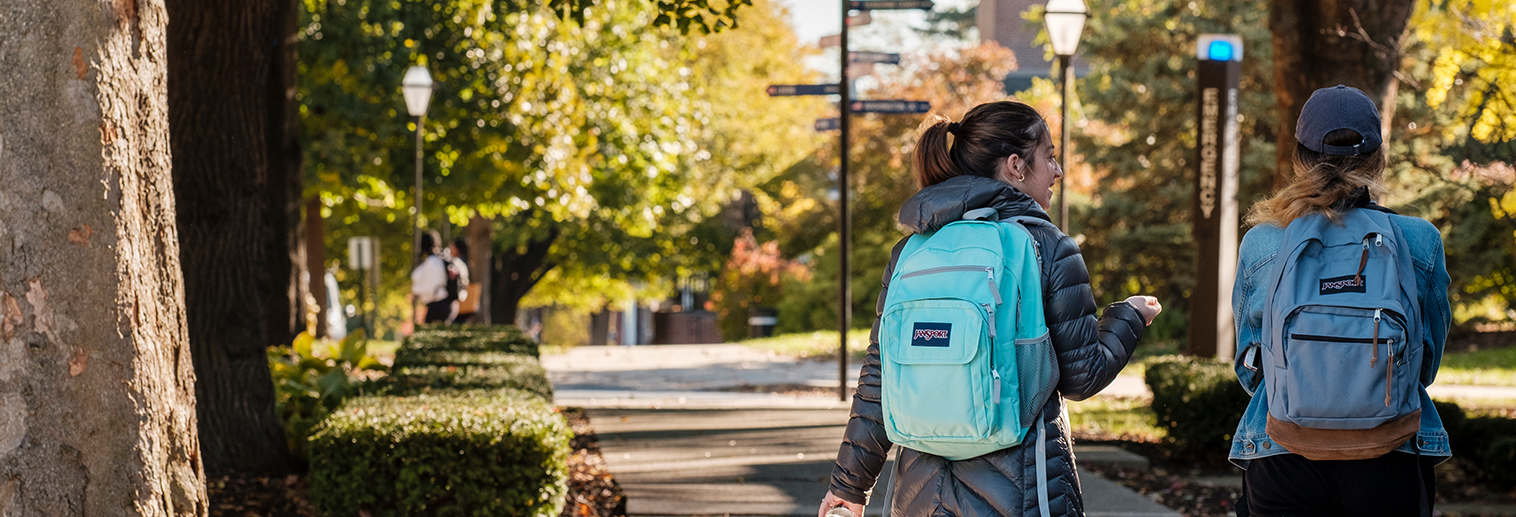 Two students walk though campus with backpacks on